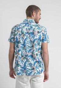 Chemise à manches courtes, boutonnée, en tissu léger avec un motif de feuilles tropicales bleu et vert vif sur fond blanc.