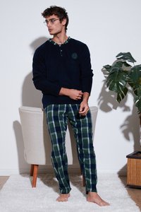 Sötétkék fleece hosszú ujjú felső, gombos kivágással, zöld és sötétkék kockás flanel nadrággal párosítva. A modell mezítláb áll egy növény mellett.