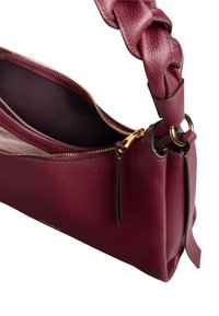 Bordeaux leren tas met een gevlochten handvat, gouden ritsdetails en een ruime binnenkant. Heeft een platte vorm en een zachte textuur.