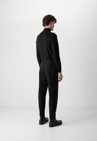 Black long-sleeve shirt with a high collar, paired with slim-fit black trousers and black ankle boots, viewed from the back.