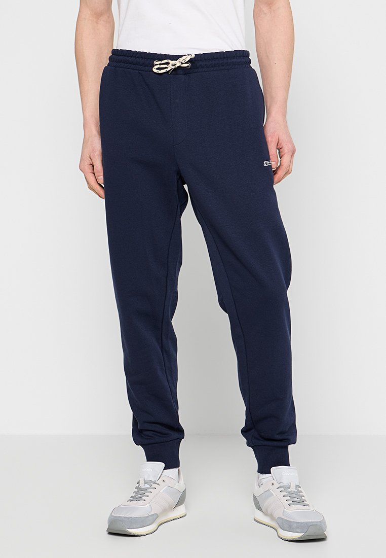 Navy blauwe joggingsbroek van zachte stof met een elastische tailleband en trekkoord. Heeft zijzakken en geribbelde boorden bij de enkels.
