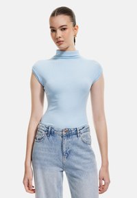 Maglietta a collo alto in blu chiaro, aderente, con maniche corte, realizzata in materiale a costine, abbinata a jeans in denim blu chiaro a vita alta.
