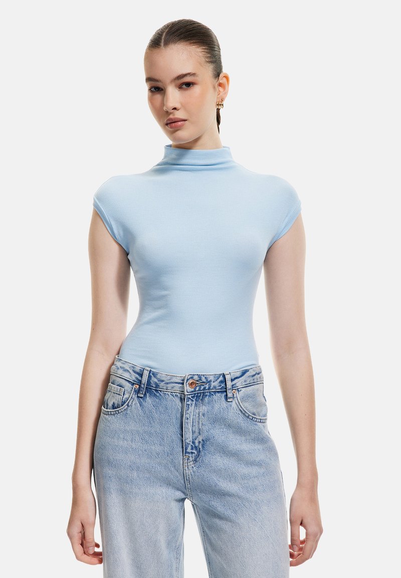Maglietta a collo alto in blu chiaro, aderente, con maniche corte, realizzata in materiale a costine, abbinata a jeans in denim blu chiaro a vita alta.