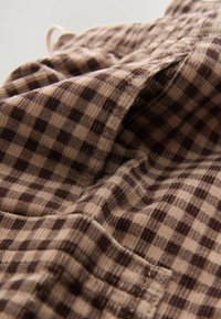 Barna és bézs kockás szövet, amely texturált felülettel rendelkezik, vízszintes és függőleges vonalakkal, bemutatva egy szőtt mintát és enyhe fényességet.