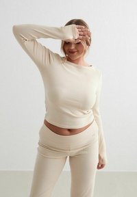 Beige ribbat långärmad topp som matchar med byxor, med en åtsittande design och textil med struktur, som framhäver en midjaöppning.