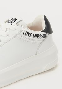 Balds ādas sporta apavi ar melnu papēdi, uz kuriem ir "LOVE MOSCHINO" zīmols uz mēles un sānu. Bieza balta zole, gluda apdare.
