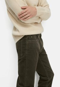 Beige ribbed sweater and dark brown corduroy pants. The sweater has a loose fit, while the pants feature side pockets and a button closure.