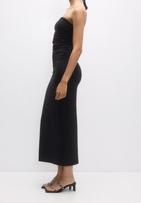 Robe noire sans bretelles avec texture froncée, tissu lisse et silhouette ajustée. Assortie à des sandales à talons noires avec des accents rayés.