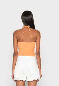 Top halter laranja com nervuras e um fecho na parte de trás, combinado com calções brancos desfiados com bainha desfiada e bolsos traseiros.