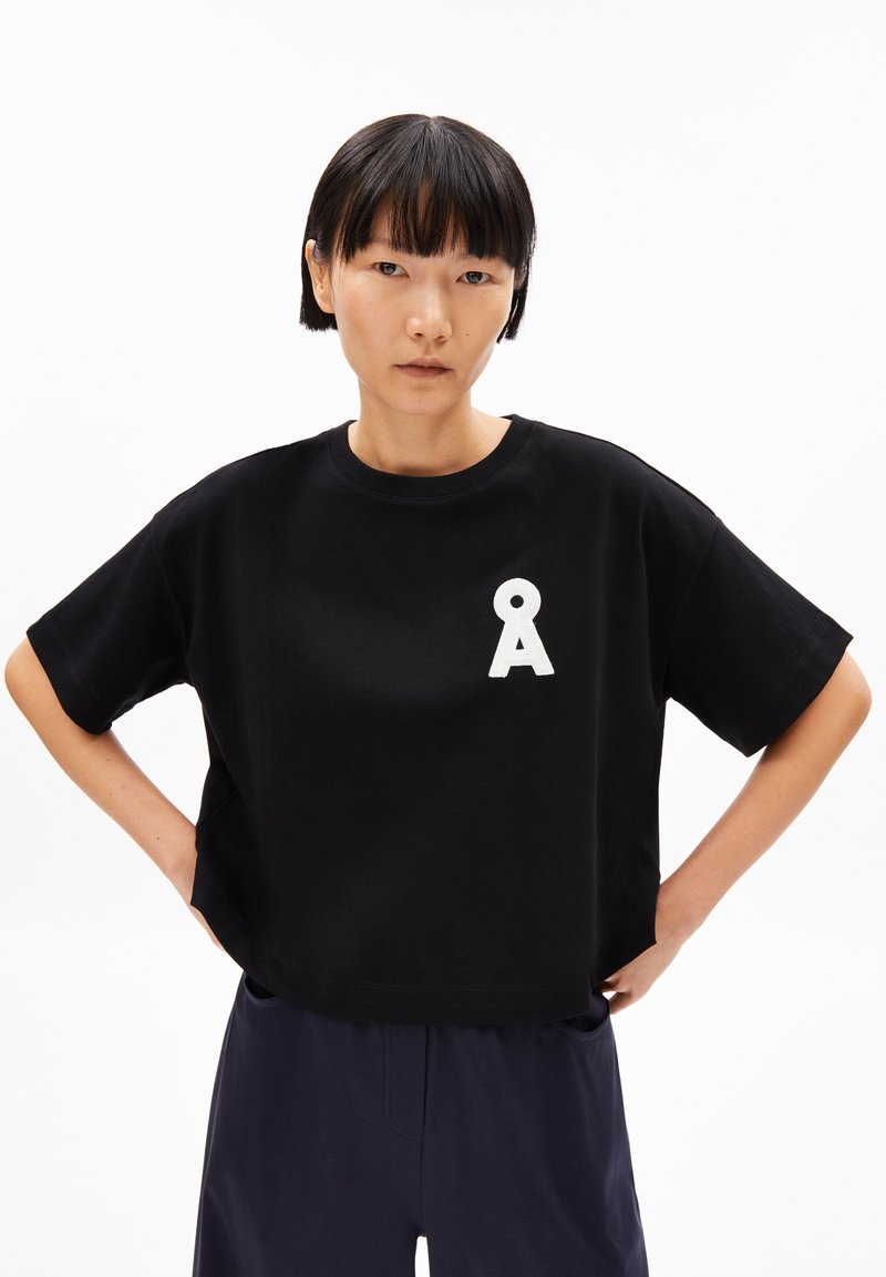 Black cropped t-shirt made of cotton; features a white letter "A" on the chest; short sleeves, relaxed fit, smooth texture.