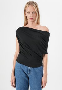 Zwarte off-shoulder top met gedrapeerd ontwerp en zachte textuur, gecombineerd met hooggetailleerde blauwe jeans.