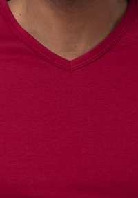 Punainen V-pääntie T-paita, joka on valmistettu pehmeästä puuvillasekoitekankaasta, jossa on sileä pinta ja hienovarainen heather-kuviointi pinnalla.