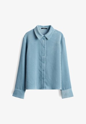 Hellblaue Cordhemd mit einer Knopfleiste vorne, Kragen und langen Ärmeln, die breite Manschetten und eine vertikale gerippte Textur aufweisen.