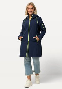 Laivaston sadeviitta, jossa on limevihreä vetoketju ja yksityiskohtia, pitkät hihat, huppu ja etutaskut, valmistettu vedenkestävästä materiaalista. Rennon mallinen.