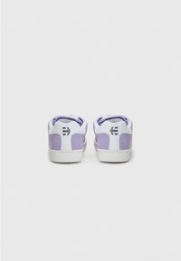White sneakers with light purple suede accents. Features a rounded toe, flat sole, padded collar, and logo on the heel.
