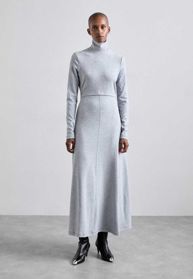 Grijze lange mouw turtleneck jurk met een aansluitend bovenstuk en een vloeiende rok, gemaakt van zachte stof. Draag met zwarte enkellaarsjes met spitse neuzen.