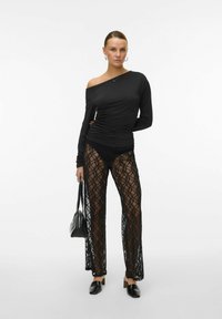 Črni dolg rokav s asimetričnim ovratnikom, v kombinaciji s prosojnimi črnimi čipkastimi hlačami z rožnatim vzorcem in prilegajočo silhueto.