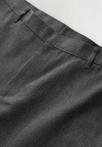 Gros plan sur la ceinture d’un pantalon en tissu gris foncé, avec passants de ceinture et une texture propre et lisse sur un fond clair.