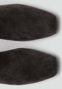 Chaussures en daim gris foncé avec une texture lisse, un bout pointu et des lignes épurées, mettant en valeur un design minimaliste sans éléments métalliques visibles.