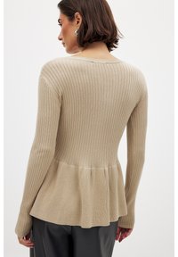 Béžový úpletový sveter s dlhým rukávom, ktorý má peplum lem, textúrovanú látku, priliehavé telo a priliehavé rukávy. Jednoduchý okrúhly výstrih na zadnej strane.