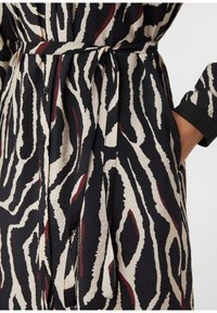 Abito a strisce zebrate in bianco e nero, con vita cintrata, bottoni sul davanti e una vestibilità comoda con maniche a risvolto.
