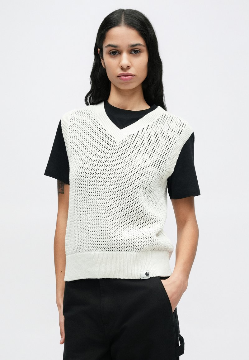 Gilet lavorato a maglia di colore grigio chiaro con trama, con scollo a V, indossato sopra una maglietta nera a maniche corte. Presenta bordi a costine e un'etichetta con logo sull'orlo.