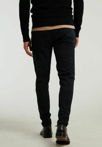 Marinblå rutiga slim-fit byxor med en slät yta och subtil lyster, tillsammans med svarta läderskor och en svart tröja.