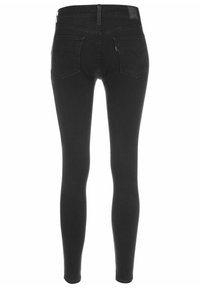 Vaqueros skinny negros de mezclilla con una textura suave. Cuenta con dos bolsillos traseros y una cinturilla alta con detalles de costura.