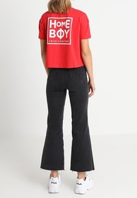Camiseta corta roja con gráfico blanco "HOME BOY LOUD COUTURE" en la parte posterior, combinada con jeans acampanados negros y zapatillas blancas.