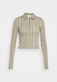 Långärmad, krageklädd topp i olivgrön och gräddvit med en halvdragkedja och schackbrädmönstrad text. Figursydd och kort modell med slät textur.