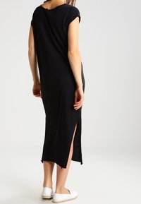 Svart, knälång klänning med sidofickor och korta ärmar. Mjuk tyg med avslappnad passform; bärs med vita slip-on skor.