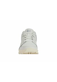 Baskets blanches en maille avec une surface texturée, des lacets et une semelle en caoutchouc beige clair. Présente un logo subtil sur la languette et des accents gris.