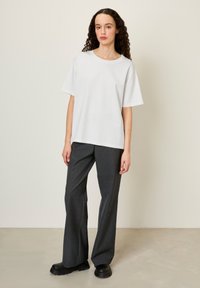 T-shirt en coton blanc avec un col rond et des manches courtes, associé à un pantalon large gris charbon et des chaussures à plateforme noires.