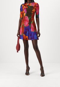 Robe à manches courtes à motifs floraux avec des couleurs vives de rose, orange et bleu, fabriquée en tissu doux ; assortie à un petit sac à main rouge et des sandales noires.