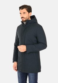 Cappotto isolato grigio scuro con cappuccio, dotato di zip frontale, tasche laterali e un design strutturato, realizzato in tessuto liscio e opaco.