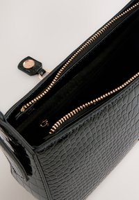 Sac à main en similicuir noir avec une surface texturée, des fermetures éclair en or rose et un intérieur spacieux présentant plusieurs compartiments.