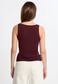 Top senza maniche color borgogna con un design aderente, caratterizzato da una texture arricciata sul retro, abbinato a pantaloni a gamba larga color bianco sporco con tasche.
