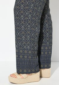 Navyblauwe gestreepte broek met een bloemendessin, met een brede zoom en subtiele textuur; gecombineerd met beige plateau-sandalen.