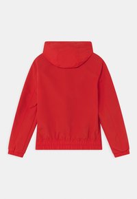 Czerwona wodoodporna kurtka z kapturem, elastycznymi mankietami i zwężaną talią. Gładka tekstura i minimalistyczny design, pokazana od tyłu.