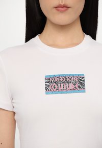 Fehér pamut póló, színes, csillogó logóval, zebramintás folttal és merész, stilizált pink és kék felirattal.
