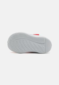 Semelle de sneaker blanche avec des motifs de grip texturés. Des accents rouges sont visibles le long des côtés. Présente des rainures et une finition lisse.