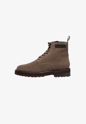 Bottines en daim marron avec un bout rond, un laçage à l'avant et un petit talon. Comprend une sangle de traction et un patch logo sur le côté.