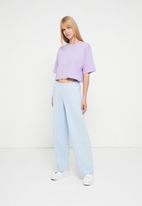 Λιλά κοντομάνικο μπλουζάκι σε κομμένη γραμμή συνδυασμένο με ανοιχτό μπλε φαρδιά φόρμα. Λευκά αθλητικά παπούτσια ολοκληρώνουν το casual ντύσιμο.