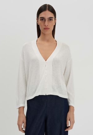 Witte cardigans met een V-hals, lange mouwen, geribbelde textuur en knoopsluiting, gecombineerd met donkerblauwe broeken. Gladde stof met een relaxte pasvorm.