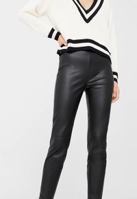 Kremowy sweter z czarnym wykończeniem, z dekoltem w kształcie litery V i długimi rękawami, w połączeniu z czarnymi spodniami z sztucznej skóry o gładkiej strukturze, dopasowany krój.