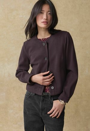 Dark purple, cropped jacket with a round neckline, front buttons, and long sleeves. Worn over a burgundy lace top and black jeans.