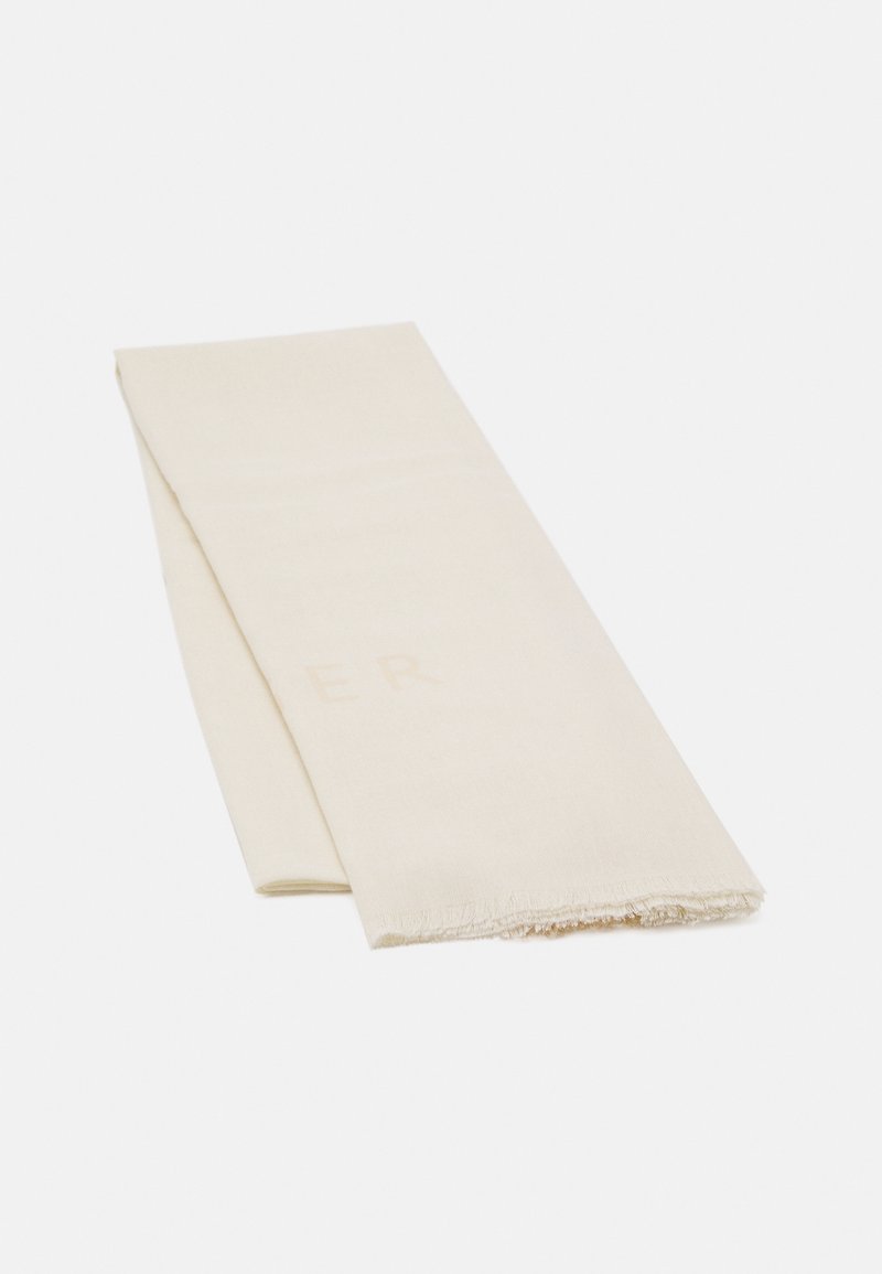 Serviette en tissu blanc cassé pliée avec une texture subtile et des bords effilochés sur un fond clair uni.