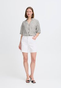 Pantalones cortos de mezclilla blanca con un corte clásico, combinados con una camisa de botones de manga corta a rayas en tonos blanco roto y gris oscuro.