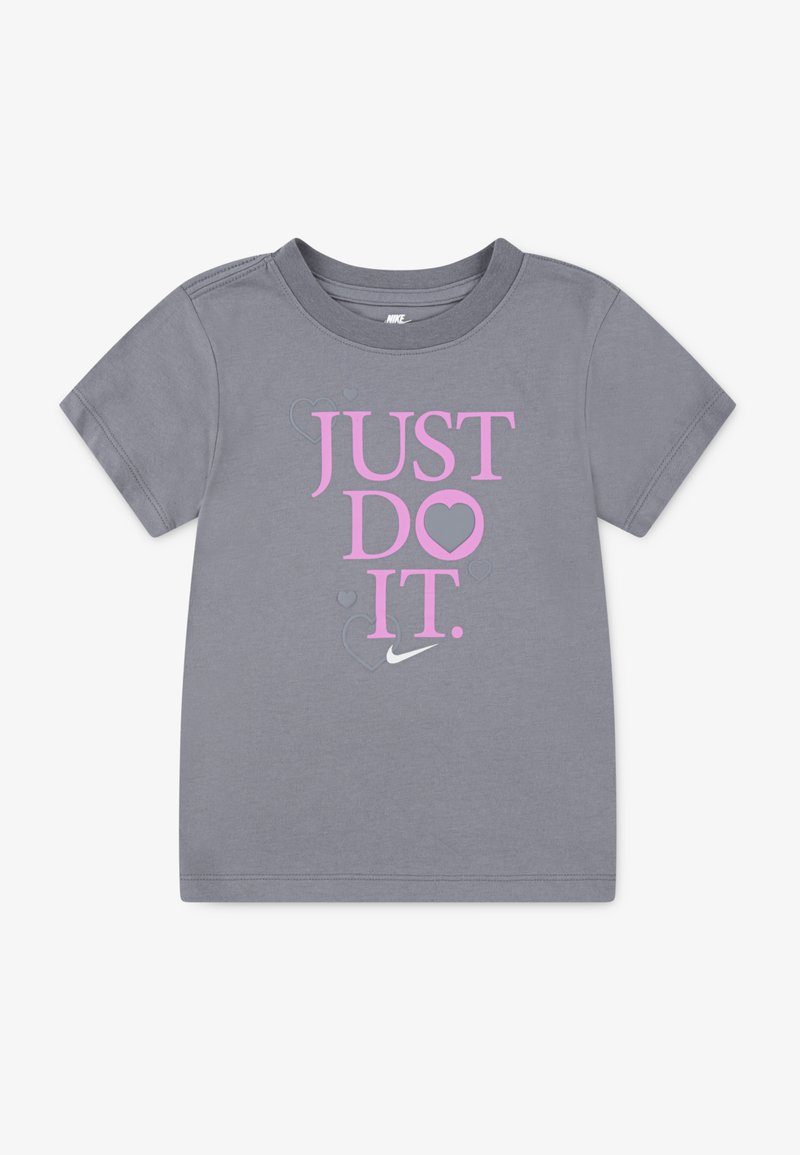 Camiseta gris de manga corta con el texto en rosa "JUST DO IT." y un gráfico de corazón junto al logo de Nike. Fabricada en suave tela de algodón.