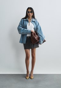 Chemise oversize en denim bleu clair, haut blanc côtelé avec détail lacé, mini jupe grise, sac en cuir marron, et escarpins pointus beiges.